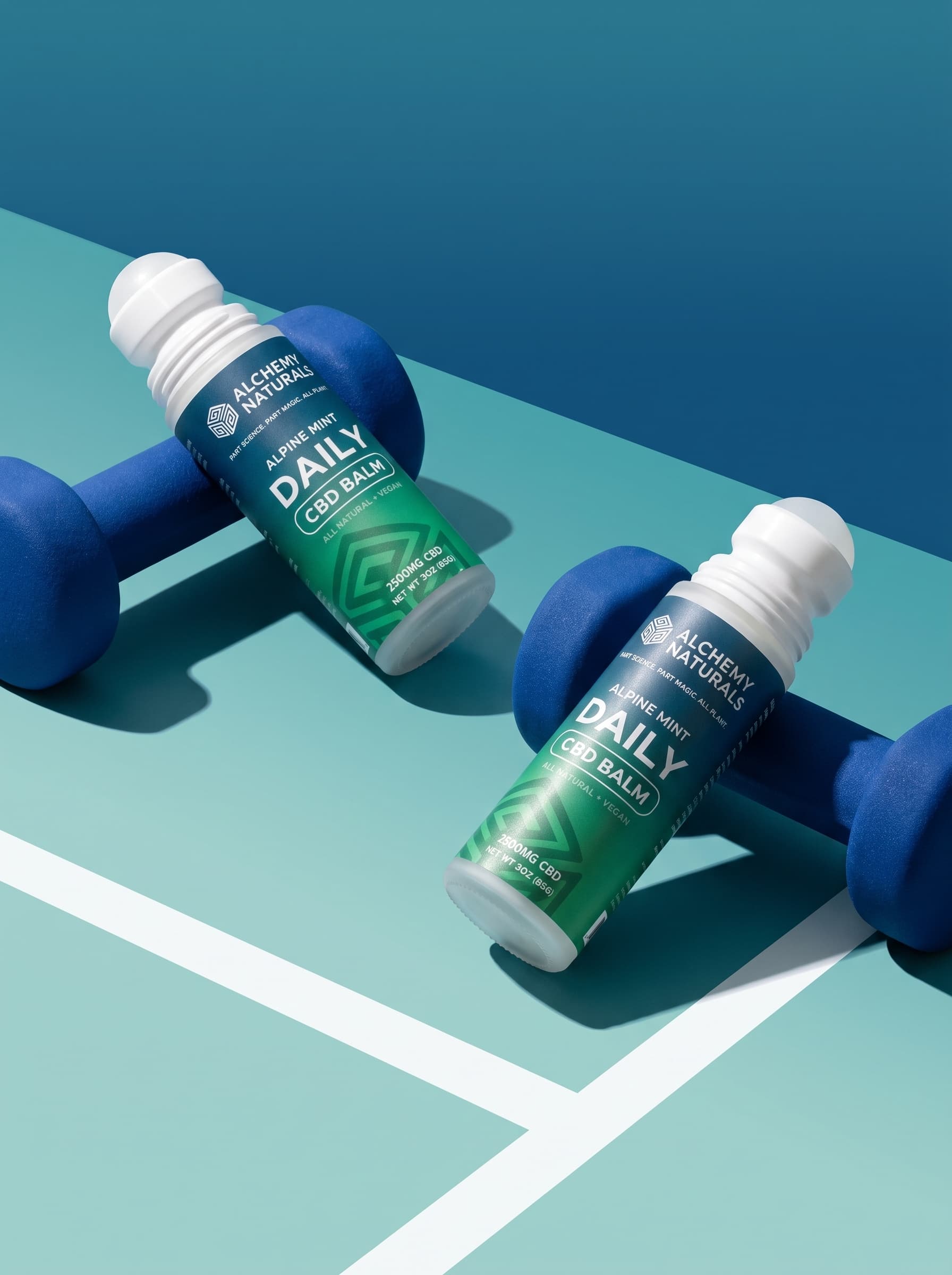 Two Alchemy Naturals Alpine Mint Daily CBD Balm roll-ons beside blue dumbbells — CBD muscle balm for post-workout recovery