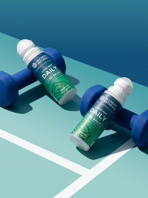Two Alchemy Naturals Alpine Mint Daily CBD Balm roll-ons beside blue dumbbells — CBD muscle balm for post-workout recovery