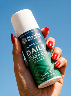 Hand holding an Alchemy Naturals Alpine Mint Daily CBD Balm roll-on against a clear blue sky